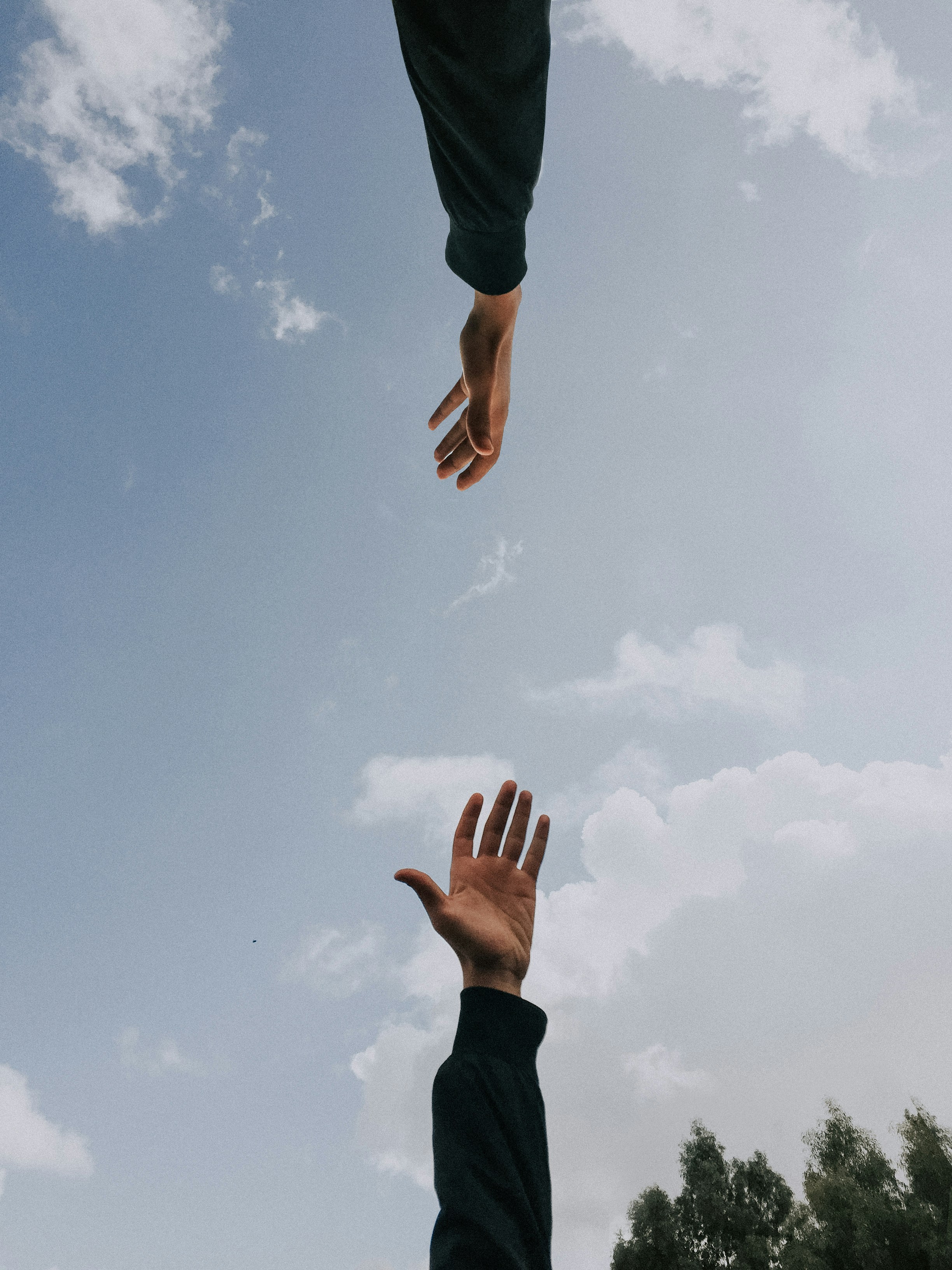 Two hands reaching for each other in front of a blue sky